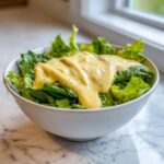 A white bowl filled with green lettuce topped generously with thick Vegan Creamy Lemon Tahini Dressing.
