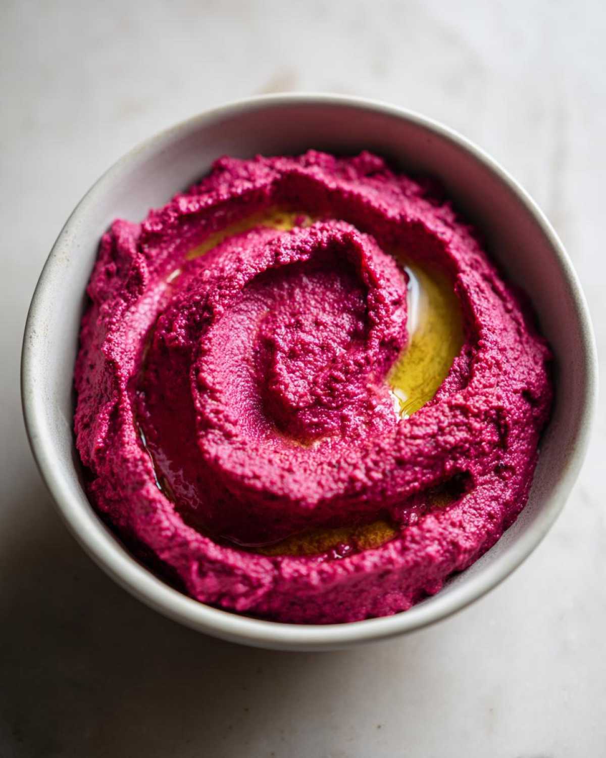 Close-up of vibrant pink Vegan Creamy Roasted Beet Hummus swirled in a bowl, drizzled with olive oil.
