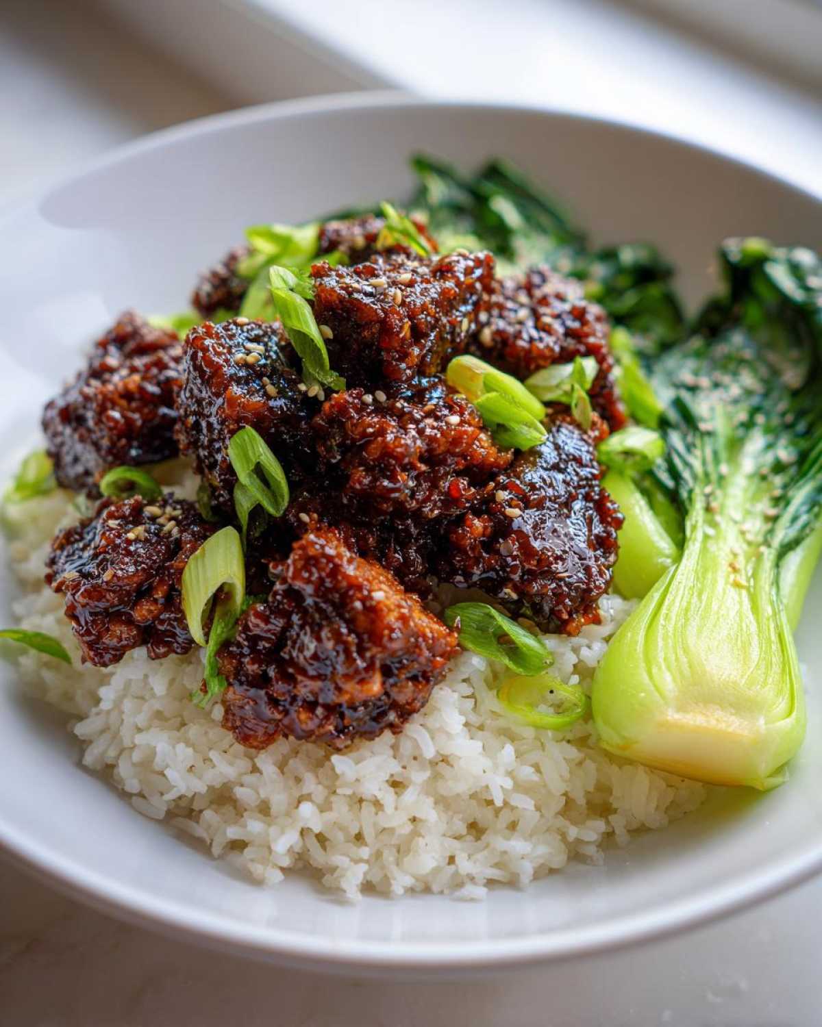 Close-up of Vegan Crispy Sesame Tempeh Bowl featuring sticky glazed tempeh over white rice with bright green bok choy.