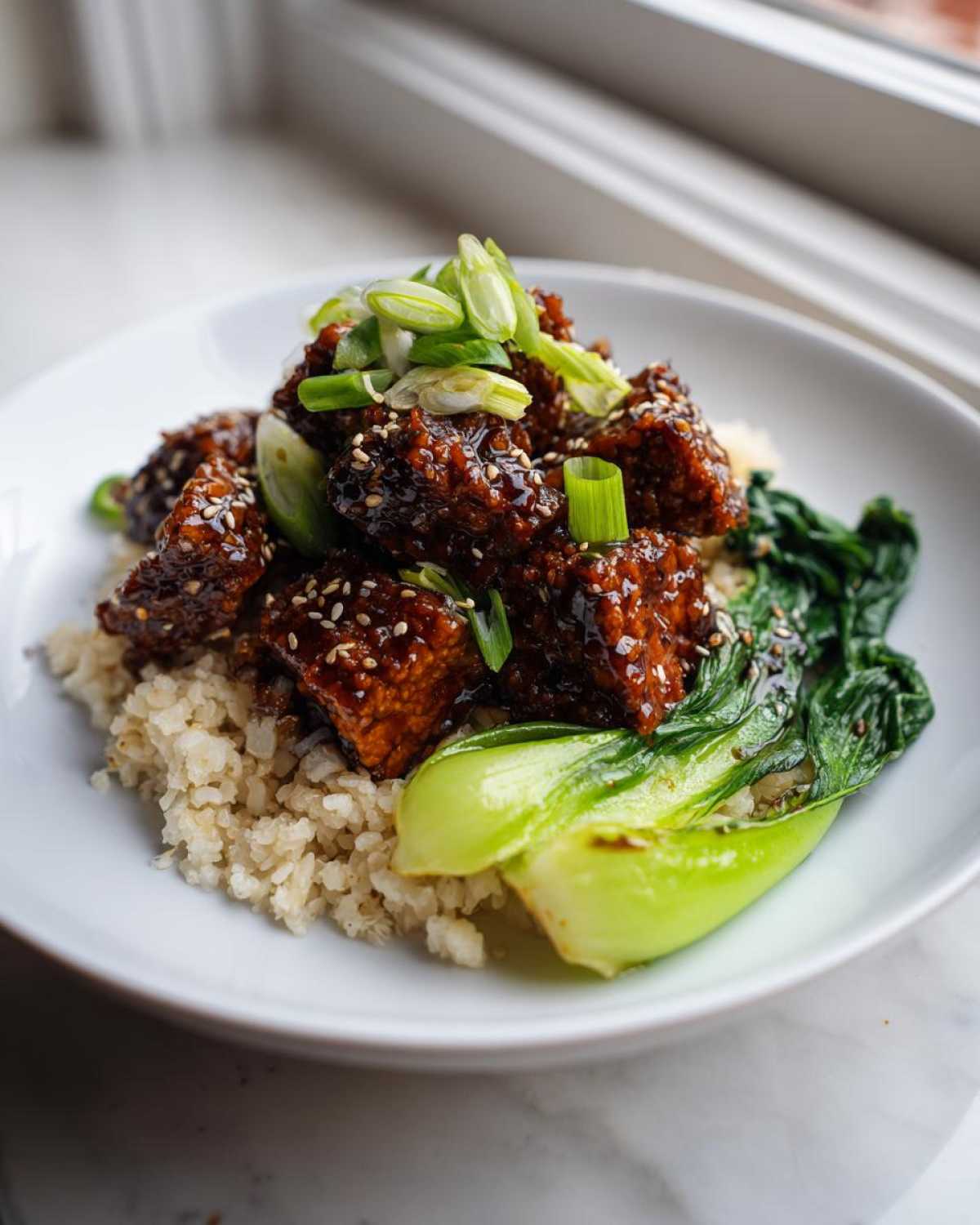 Close-up of a Vegan Crispy Sesame Tempeh Bowl served over rice with bok choy and green onions.