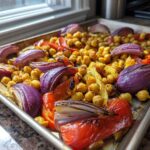 Close-up of roasted chickpeas, red onion wedges, and bell peppers on a sheet pan for Vegan One-Pan Chickpea Shawarma.
