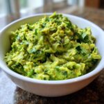 Close-up of chunky, vibrant green guacamole topped with fresh cilantro in a white bowl.