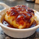 Close-up of a piece of baked cod covered in a thick, shiny honey garlic sauce, served in a small white ramekin.