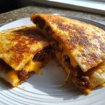Two halves of a golden-brown Cheesy Ground Beef Quesadillas, oozing melted cheese and savory ground beef filling, served on a white plate.