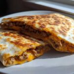 Two halves of a golden-brown Cheesy Ground Beef Quesadillas, showing melted cheese and seasoned ground beef filling.