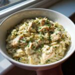 A close-up of a white bowl filled with creamy Chicken Alfredo with Orzo Pasta, topped with fresh parsley.