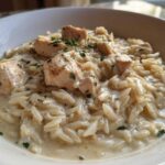 A close-up of creamy Chicken Alfredo with Orzo Pasta topped with chunks of seasoned chicken and fresh parsley.