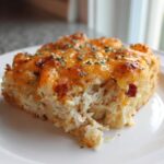 A thick slice of Chicken Bacon Ranch Tater Tot Casserole with melted cheddar cheese and herbs on a white plate.