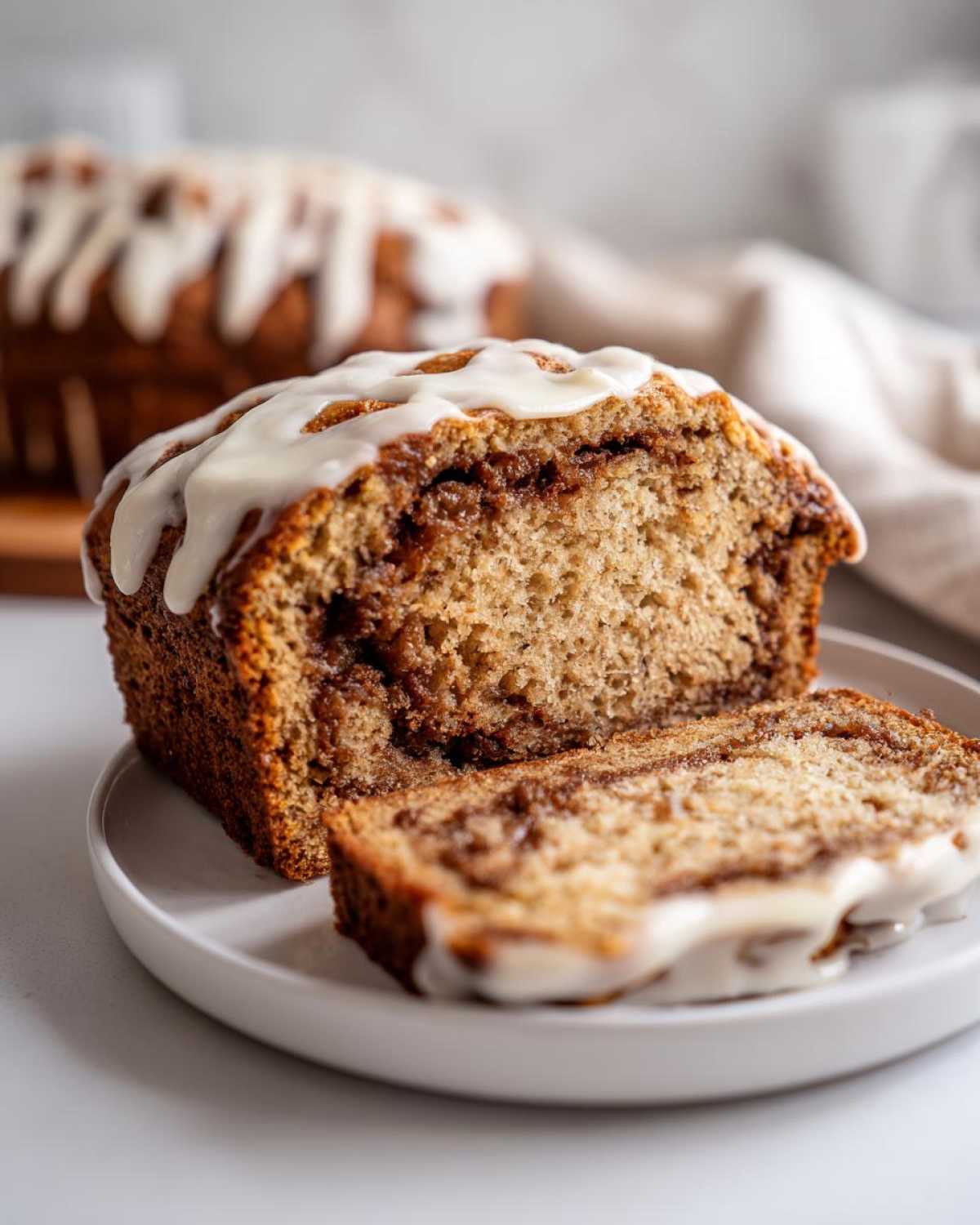 Close-up of a sliced Cinnamon Roll Banana Bread Loaf topped with thick white icing.