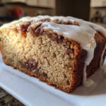 Close-up of a thick slice of Cinnamon Roll Banana Bread Loaf topped with dripping vanilla icing.