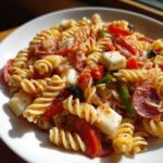 Close-up of Cold Pasta Salad with Italian Dressing featuring rotini, mozzarella cubes, pepperoni, and tomatoes.