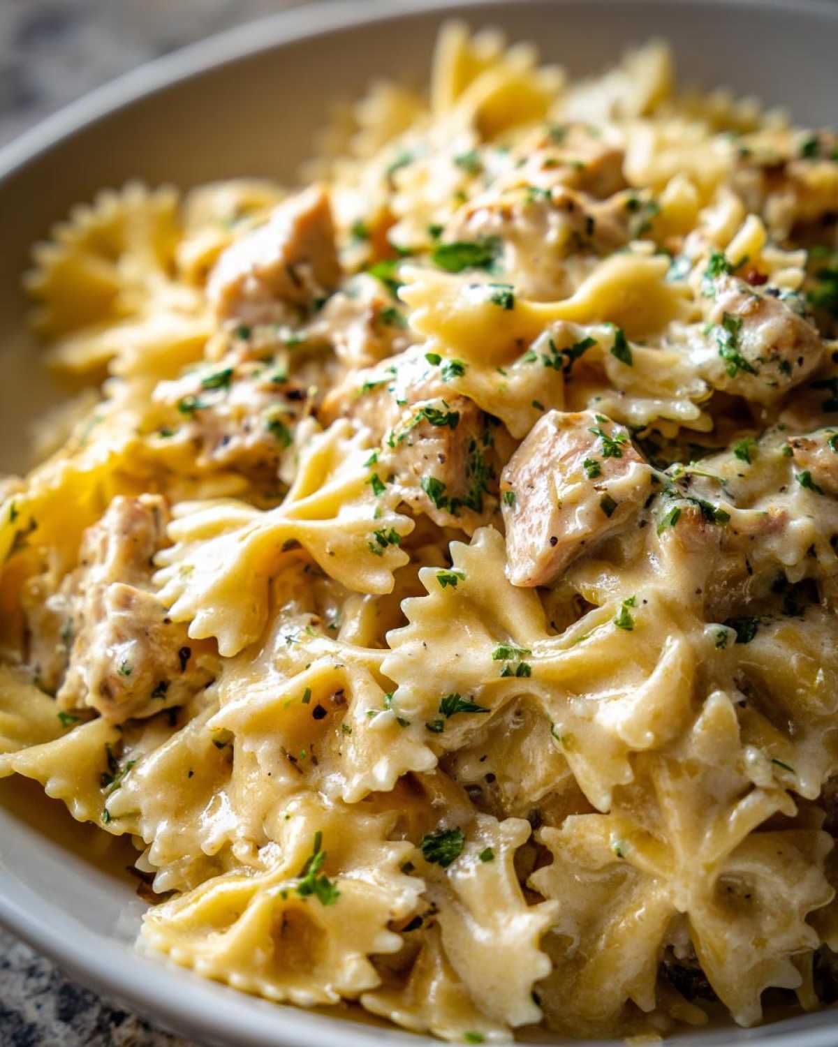 Close-up of creamy Cowboy Butter Lemon Bowtie Chicken pasta dish topped with fresh parsley.