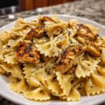 Close-up of creamy bowtie pasta topped with grilled chicken pieces seasoned with herbs, showcasing the Cowboy Butter Lemon Bowtie Chicken.