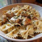 A white bowl filled with Cowboy Butter Lemon Bowtie Chicken pasta coated in a creamy herb sauce.