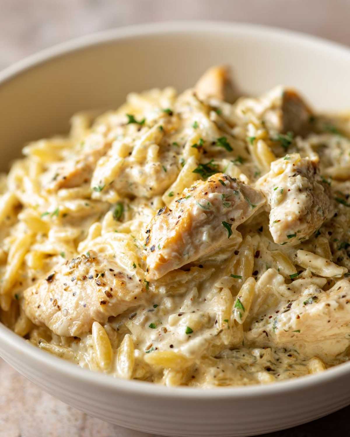 Close-up of creamy Chicken Alfredo with Orzo Pasta, topped with seasoned chicken pieces and fresh parsley.