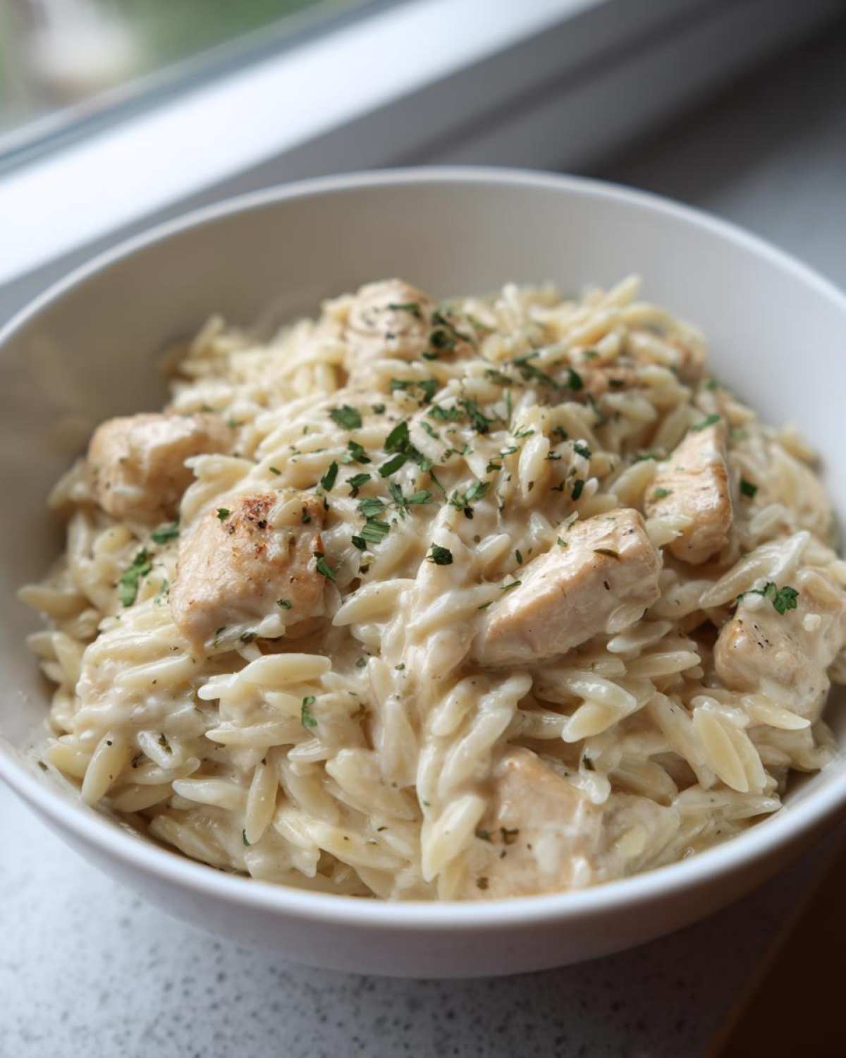 Close-up of creamy Chicken Alfredo with Orzo Pasta topped with fresh parsley in a white bowl.