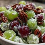 A close-up of a bowl filled with vibrant green and red grapes coated in a creamy dressing, topped with crunchy pecans, showcasing the finished Grape Salad.