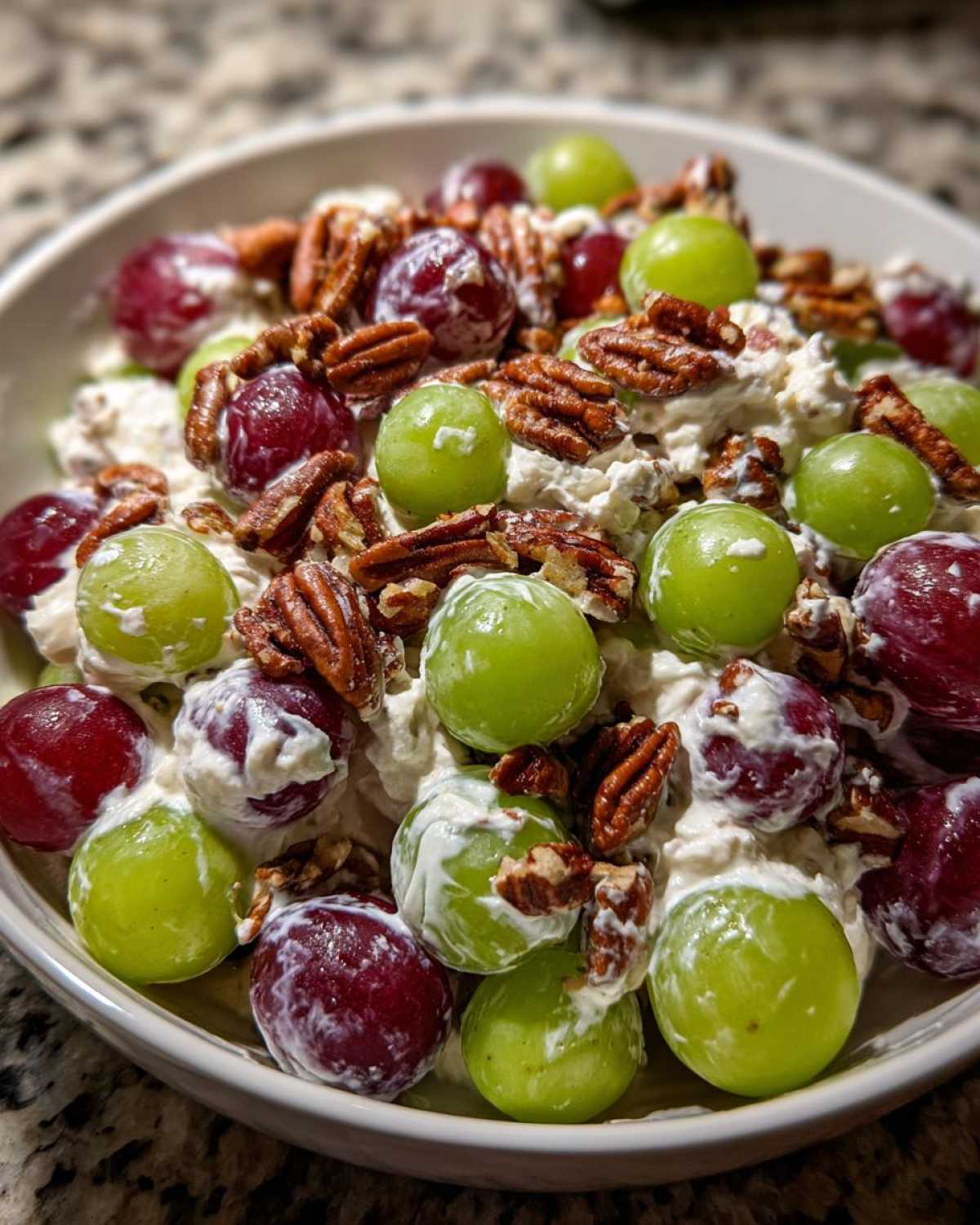 A close-up view of a creamy Grape Salad mixed with red and green grapes and topped with crunchy pecans.
