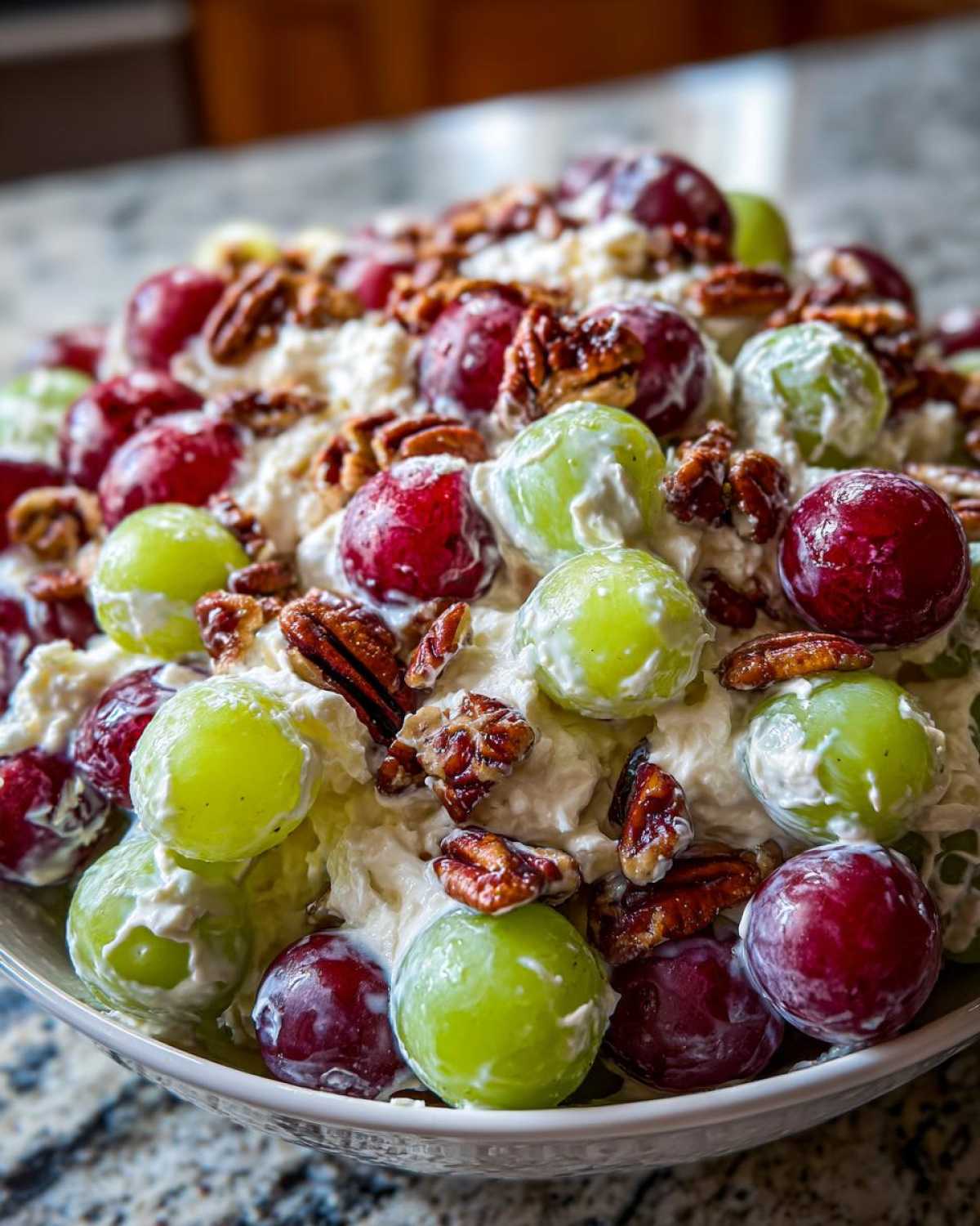 A close-up bowl filled with creamy Grape Salad featuring red and green grapes coated in a white dressing and topped with crunchy pecans.