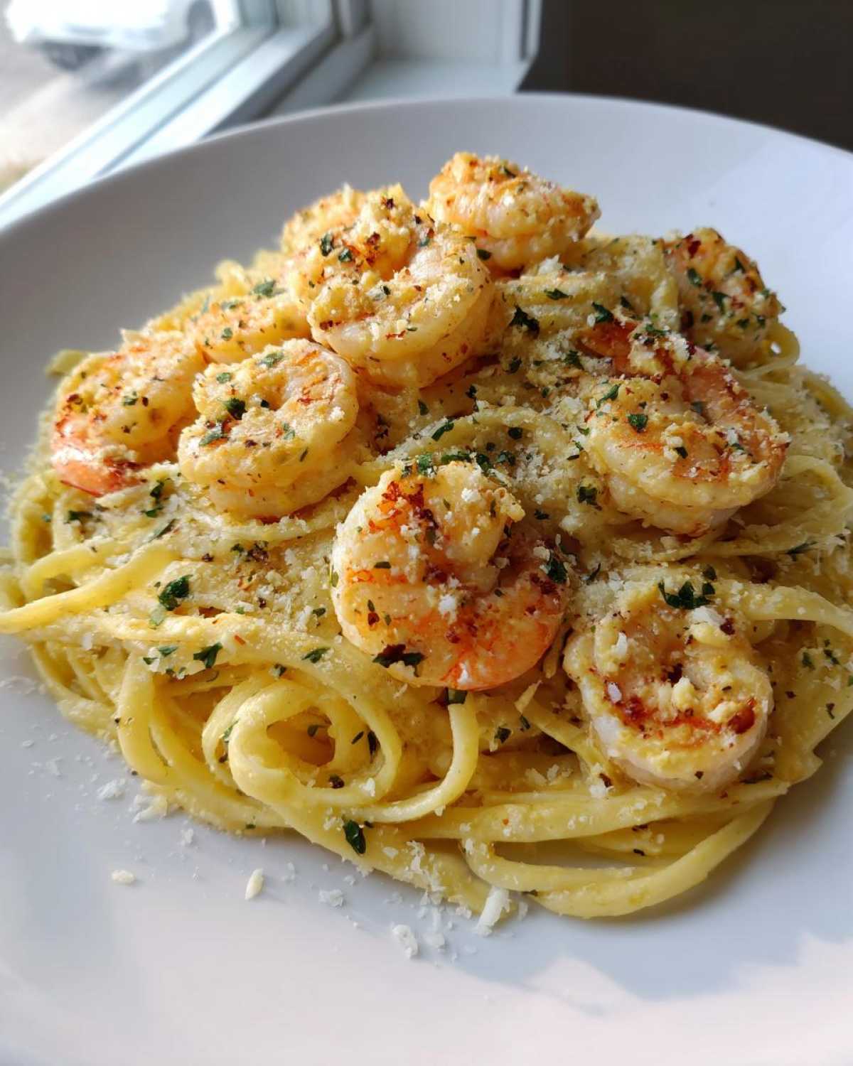 A close-up of a serving of Creamy Lemon Shrimp Pasta topped with seasoned shrimp and grated Parmesan cheese.