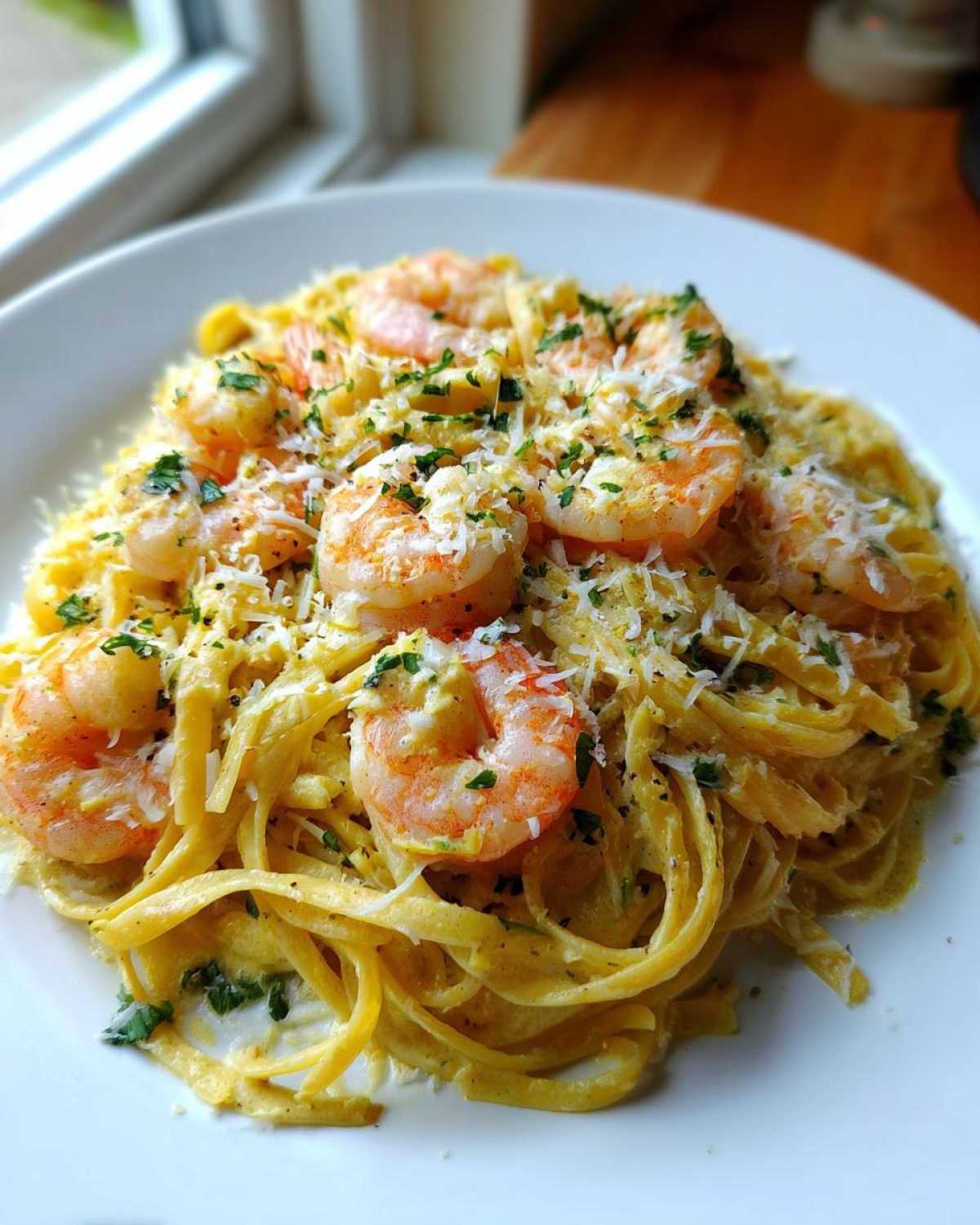 A close-up of a white plate piled high with Creamy Lemon Shrimp Pasta, topped with large shrimp and grated Parmesan cheese.