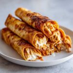 A stack of golden brown, crispy oven rolled chicken taquitos showing shredded chicken and creamy filling.