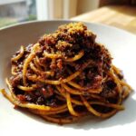 A close-up, appetizing photo of a mound of Dirty Spaghetti coated in a dark, rich sauce and topped with toasted breadcrumbs.