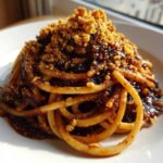A close-up of a serving of Dirty Spaghetti coated in a dark, rich sauce and generously topped with golden brown crumbs.