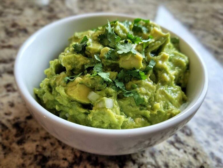A close-up of chunky, bright green guacamole topped with fresh cilantro in a white bowl.