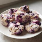A white plate holds several mounds of Frozen Blueberry Greek Yogurt Clusters mixed with vibrant purple blueberries.