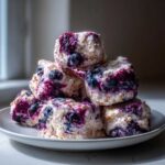 A stack of homemade Frozen Blueberry Greek Yogurt Clusters on a white plate, showing visible blueberries.