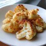 Close-up of crispy, golden-brown Garlic Butter Roasted Cauliflower florets served on a white plate.