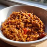 A close-up of a white bowl filled with rich Ground Beef Orzo in Tomato Sauce, glistening under natural light.