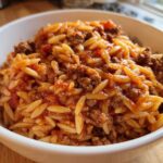 Close-up of a white bowl filled with savory Ground Beef Orzo in Tomato Sauce, featuring rice-shaped pasta and seasoned ground meat.