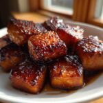 Close-up of perfectly caramelized Honey Garlic Salmon Bites glistening with a thick, dark glaze on a white dish.