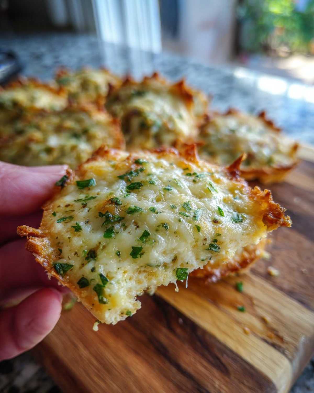 A hand holding one cheesy Ritz Cheese Bites topped with melted cheese and fresh parsley.