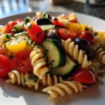 Close-up of a serving of colorful Pasta Salad featuring fusilli pasta, cherry tomatoes, zucchini slices, and black olives.