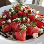 Close-up of a vibrant Watermelon Salad featuring cubed watermelon, crumbled feta cheese, fresh mint, and a balsamic glaze drizzle.