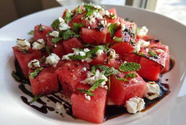 Close-up of a vibrant Watermelon Salad featuring cubed watermelon, crumbled feta cheese, fresh mint, and a balsamic glaze drizzle.