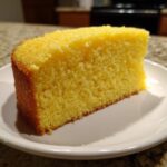 A close-up of a moist, bright yellow slice of Yellow Velvet Cake resting on a white plate.
